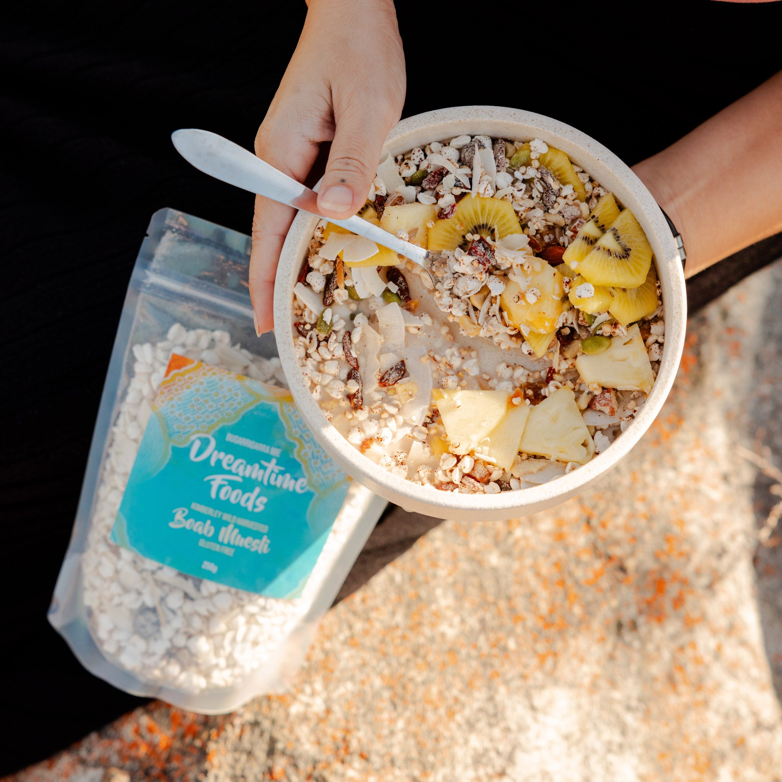 Person holding a bowl of cereal with fruit on a textured surface